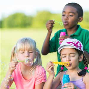 three kids blowing bubbles in a grassy field